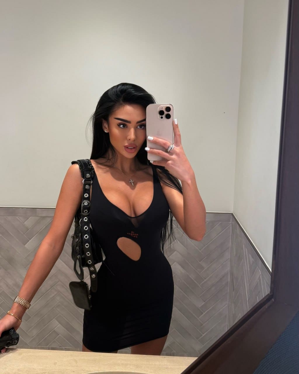 Mirror selfie showing a tight black mini dress with plunging neckline, mesh panel, cutout, and studded bag.